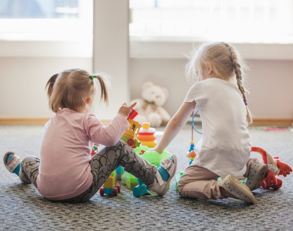 Dwie dziewczynki siedzą na podłodze w żłobku i bawią się kolorowymi zabawkami